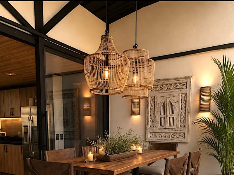 Comedor cubierto de la cabaña Beto con lámparas colgantes en fibra natural y vista hacia la cocina